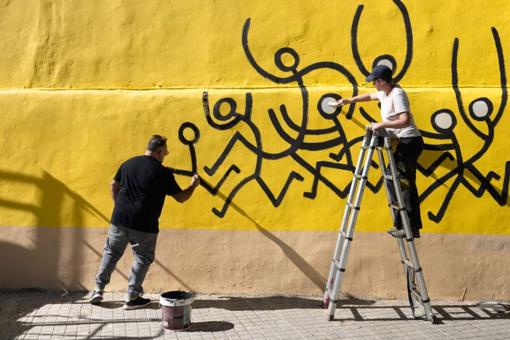 Javirroyo i l'assistent pinten alhora els personatges del mural, una des d'una escala, mural CASA NOSTRA, Barcelona, Rebobinart 2026