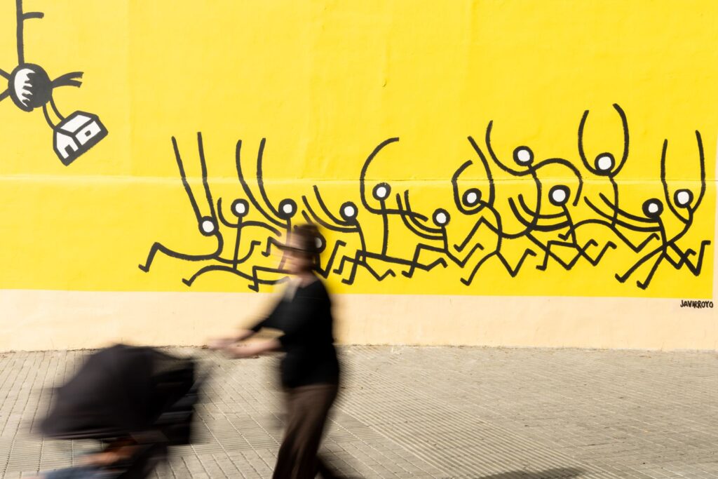 Una persona passa amb un cotxet de nadó davant de la multitud que corre del mural, CASA NOSTRA de Javirroyo, Barcelona, Rebobinart 2026