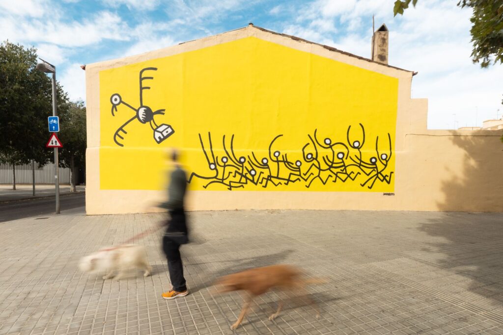 Una veïna passeja els gossos davant del mural acabat del voltor i la casa, CASA NOSTRA de Javirroyo, Barcelona, Rebobinart 2026