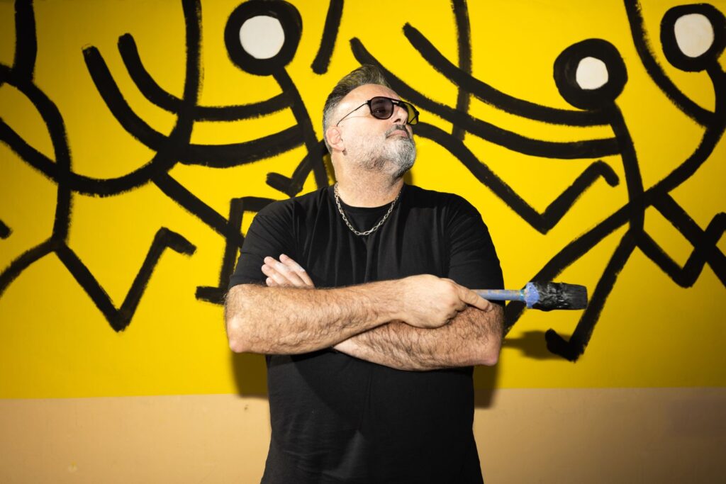 Retrat de Javirroyo amb els braços creuats davant del seu mural groc i negre, CASA NOSTRA, Barcelona, Rebobinart 2026