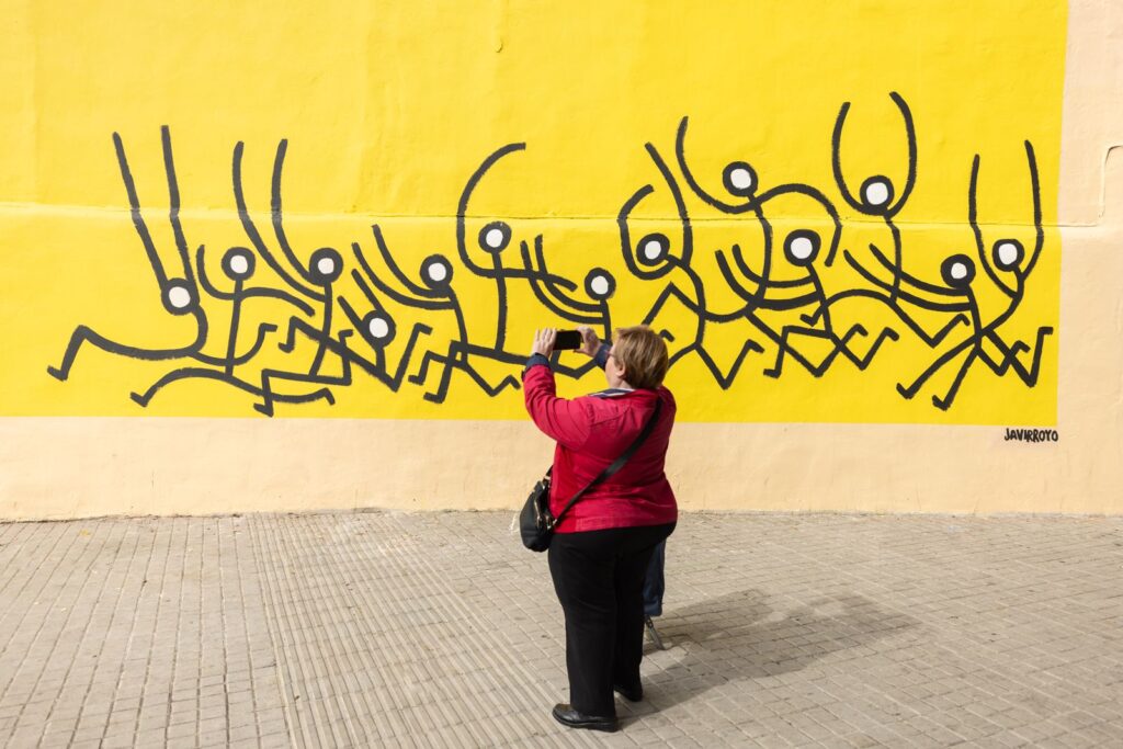 Una veïna fa una foto amb el mòbil al mural de Javirroyo, CASA NOSTRA, Barcelona, Rebobinart 2026