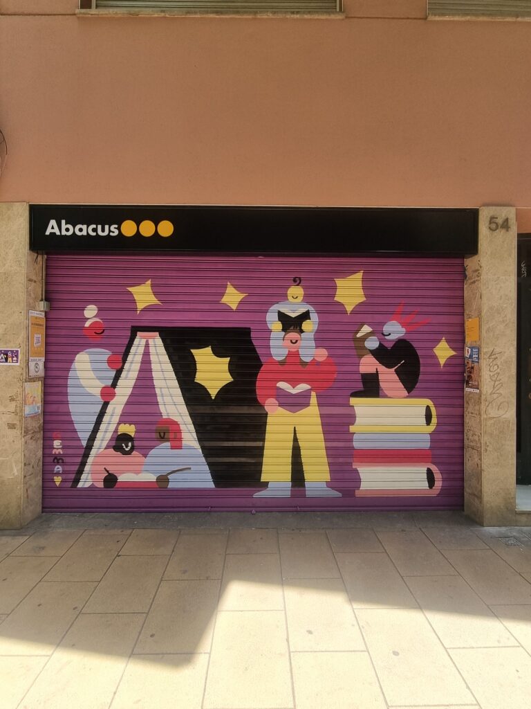 Persiana de Abacus pintada por Gemma Fontanals con tres figuras leyendo, una dentro de una cabaña de libros y otra sentada sobre una pila de volúmenes, sobre fondo rosa — Persianes que fan barri, Sant Andreu, Barcelona, Rebobinart 2026