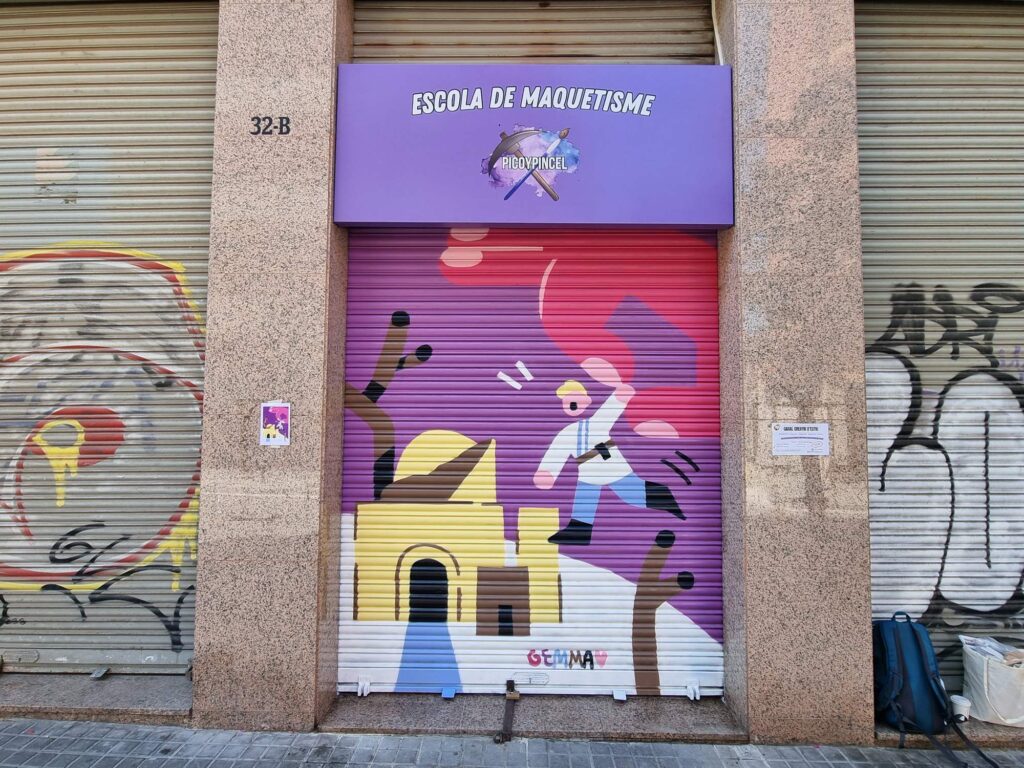 Persiana de la Escola de Maquetisme Picoypincel pintada por Gemma Fontanals con una figura pintando con pincel la maqueta de un edificio amarillo con arcada, sobre fondo magenta — Persianes que fan barri, Sant Andreu, Barcelona, Rebobinart 2026